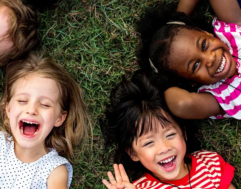 Three young children of different ethnicities lying on the grass, smiling and laughing together