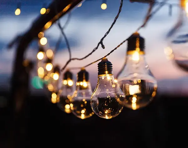 Decorative string lights with glowing bulbs hanging outdoors at dusk, creating a warm atmosphere.